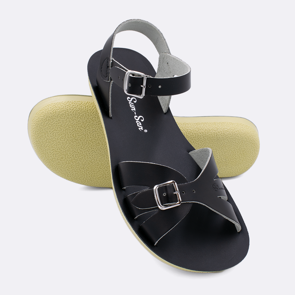 Two Women's sized 1900 Boardwalk style sandals with black straps and black insoles.  One standing with the sole facing the camera. The second is laying diagonally over the top left edge of the sole.