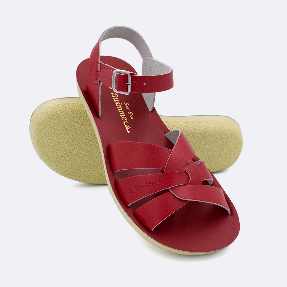 Two women's sized 8000 Swimmer style sandals with red straps and red insoles.  One standing with the sole facing the camera. The second is laying diagonally over the top left edge of the sole.